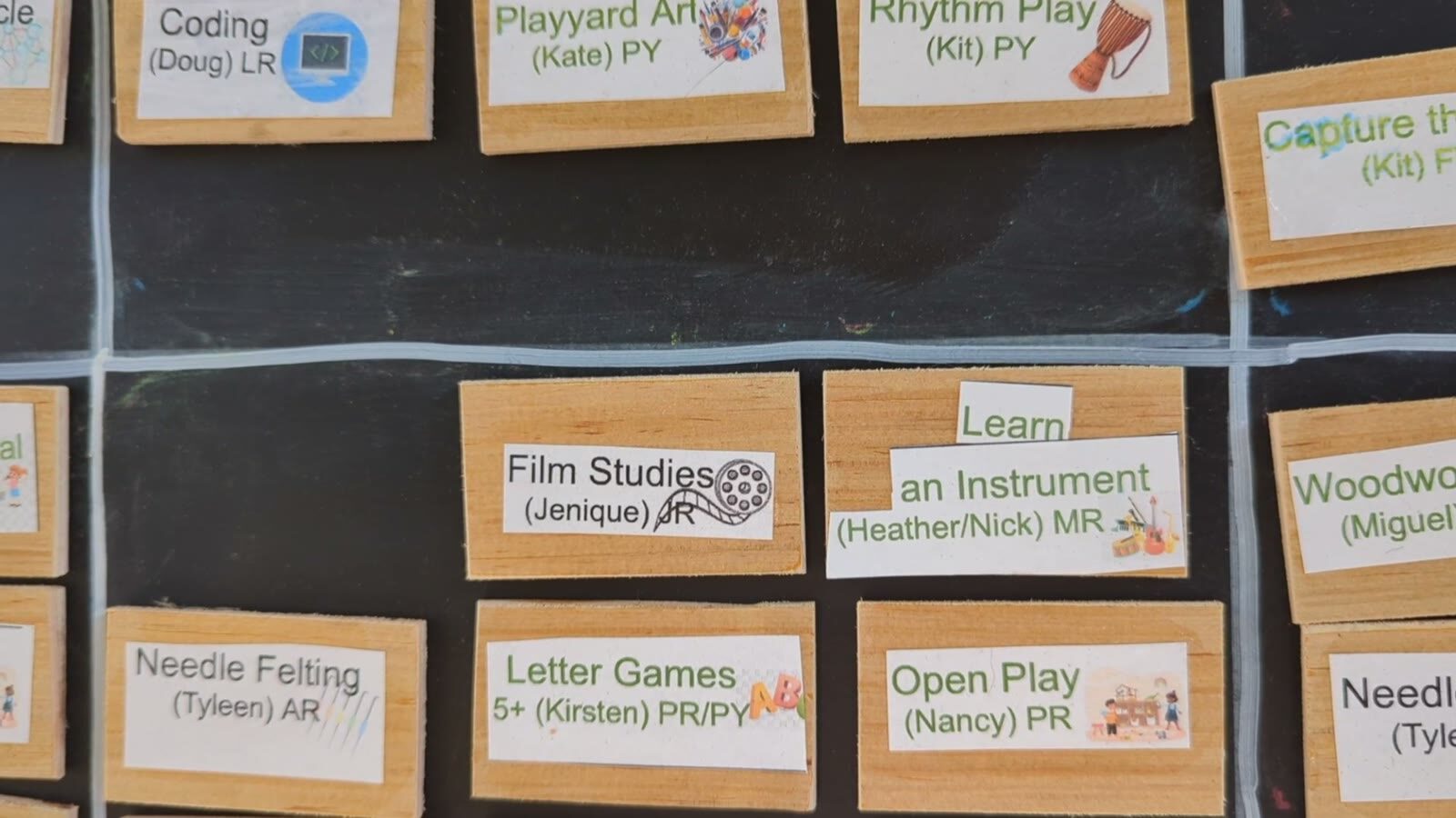 The weekly offerings board: cards for Film Studies, Learn an Instrument, Needle Felting, Letter Games, Open Play and more