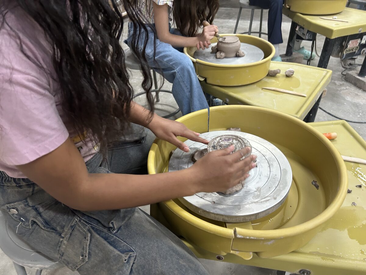Hands shaping clay on a pottery wheel